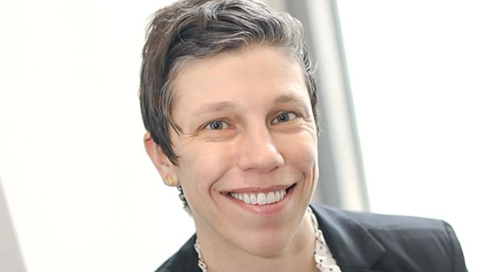 Woman with short hair smiles, sitting in brightly lit area smiles at camera