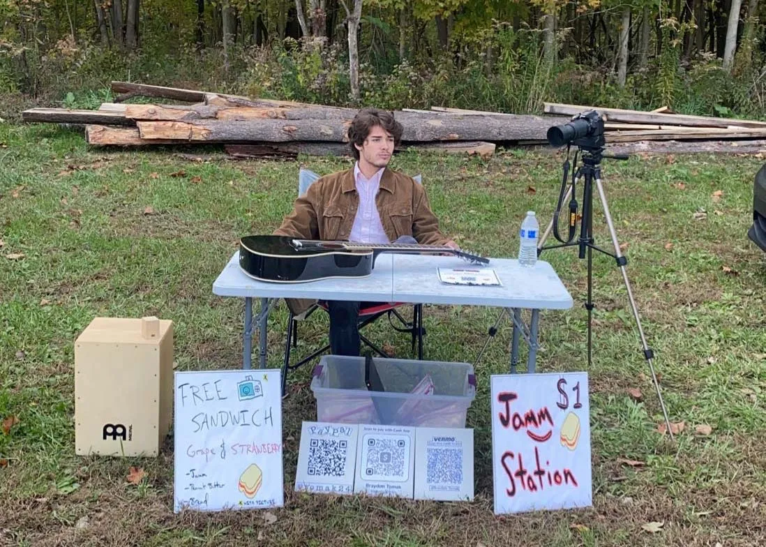 Man at table in woods with signs and guitar