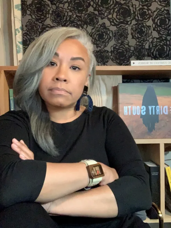 gloria wilson sits in front of bookshelf and tapestry