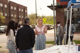 People speak outside in front of tent and brick buildings